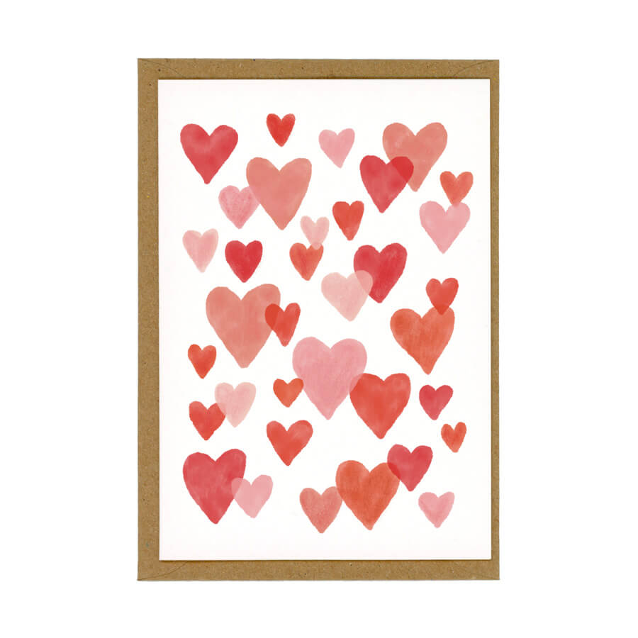 An eco-friendly greeting card of red and pink overlapping hearts on a white card sitting on top of a brown envelope
