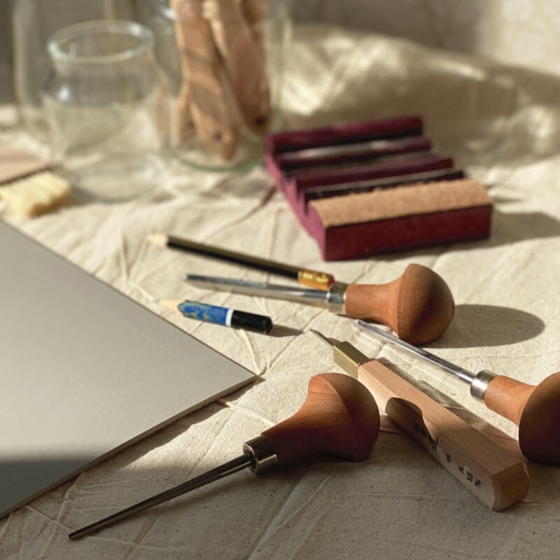 A collection of cutting tools, pencils and brushes with a block of compostable lino used to create sustainable linocut prints