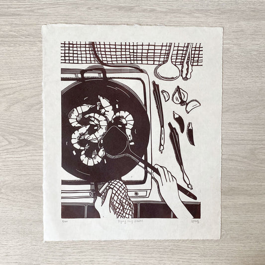 A original block print, handprinted in dark brown ink on Awagami Kitakata washi paper, of a typical kitchen scene - frying king prawns in a wok, with surrounding aromatics. An original block print by Bert and Roxy