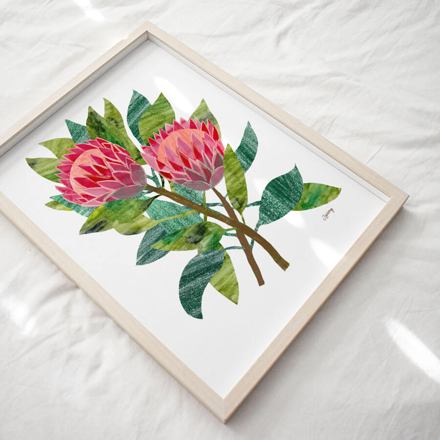 A digital reproduction of a papercut collage of two protea flowers by Bert and Roxy. Displayed in a frame on a white cloth background