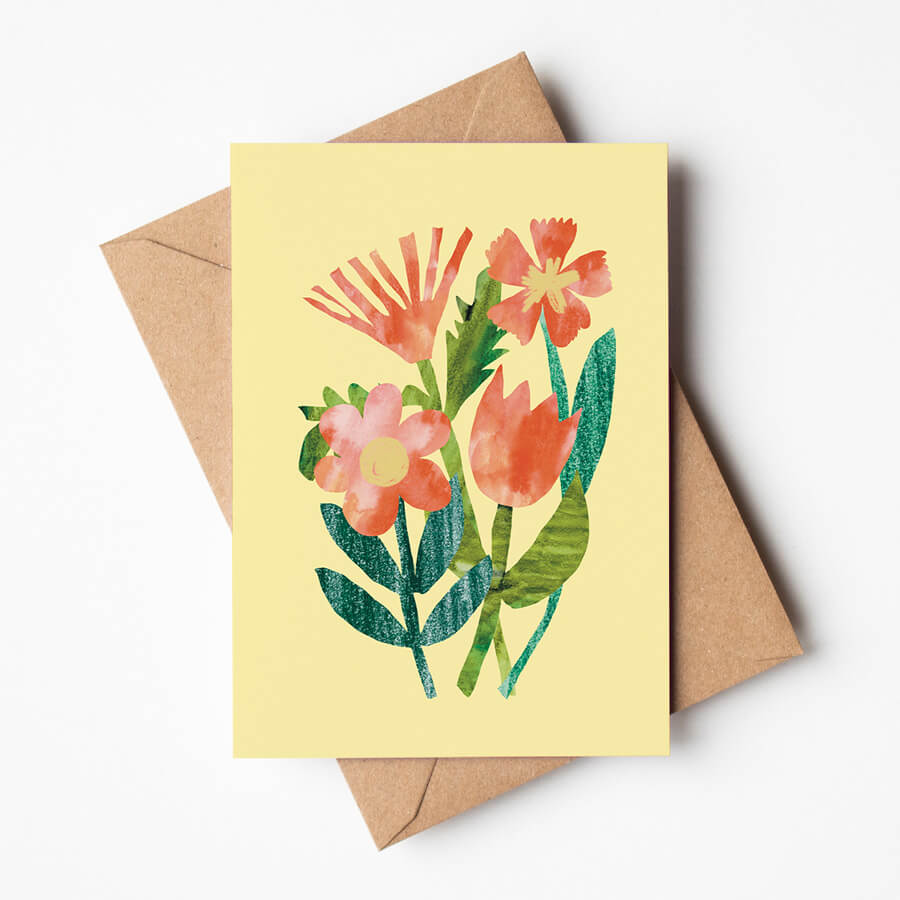 A eco friendly greeting card with 4 collage flowers on it in shades of pink and red. On a background of yellow. The card sits on top of a brown envelope.