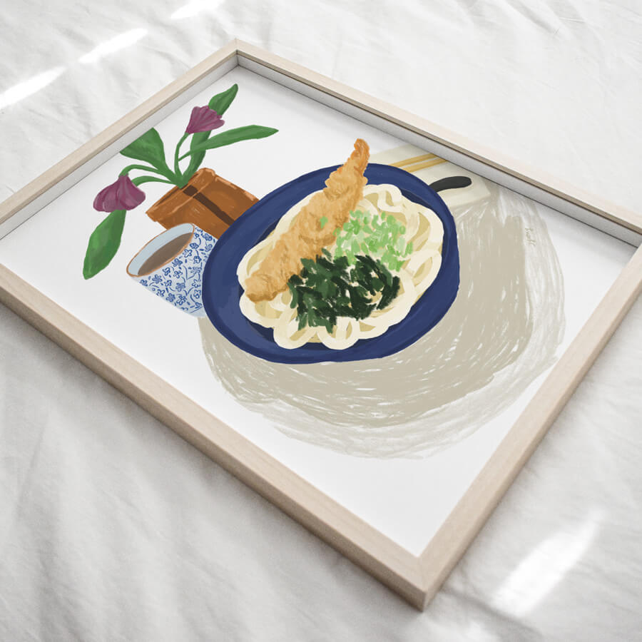 An angled view of a framed sustainably made giclee of a bowl of Japanese udon noodles topped with prawn tempura